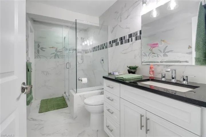 Bathroom featuring a marble finish shower, vanity, tile walls, and light marble finish floors