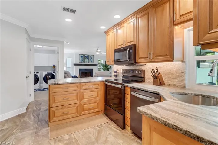 Kitchen with a fireplace, stainless steel appliances, a peninsula, light stone counters, and crown molding