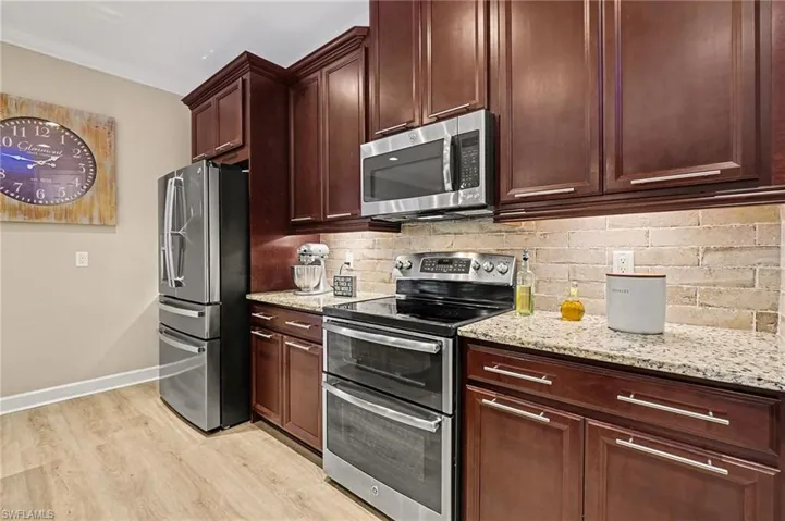 Kitchen featuring appliances with stainless steel finishes, light stone counters, light wood-style flooring, decorative backsplash, and dark brown cabinetry