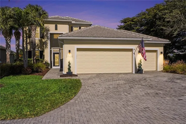 View of front of property with decorative driveway, stucco siding, a garage, a lawn, and a tiled roof