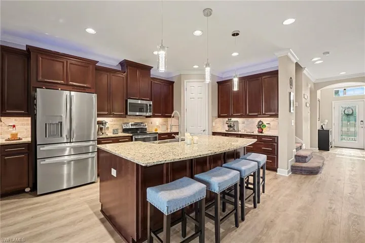 Kitchen with appliances with stainless steel finishes, a kitchen bar, dark brown cabinetry, light stone countertops, and a kitchen island with sink