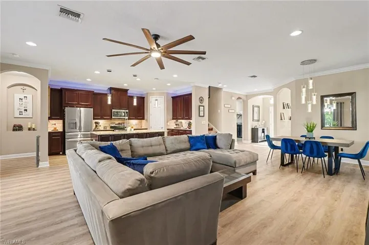 Living room featuring arched walkways, crown molding, ceiling fan, light wood finished floors, and recessed lighting