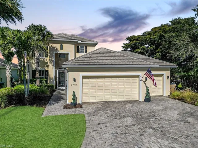 Stucco exterior residence with a two-car garage featuring a tile roof, paved driveway, and mature landscaping