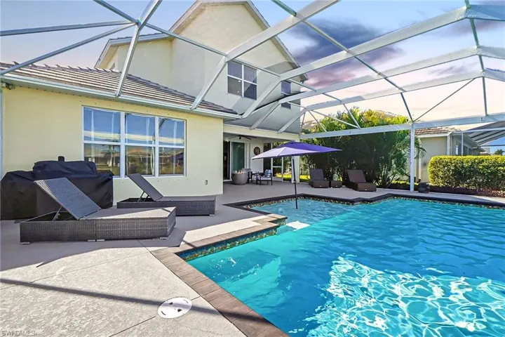 Screened swimming pool enclosure with a geometric pool, surrounding concrete patio, and exterior stucco finish