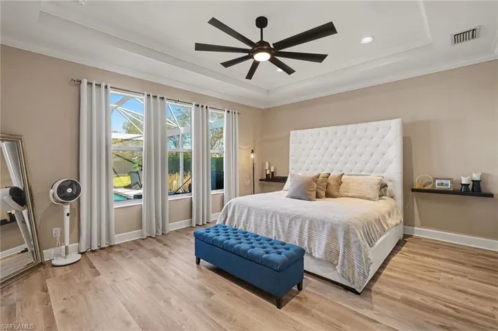 Bedroom featuring light wood-type flooring, ceiling fan, crown molding, and a raised ceiling