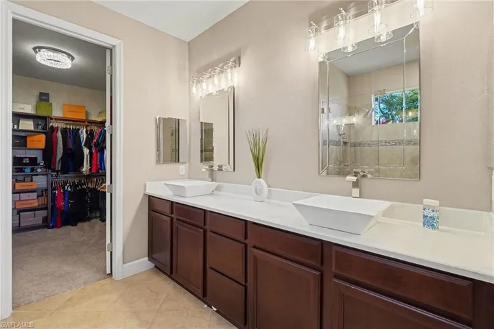 Bathroom with tiled shower, double vanity, a spacious closet, light carpet, and light tile patterned floors