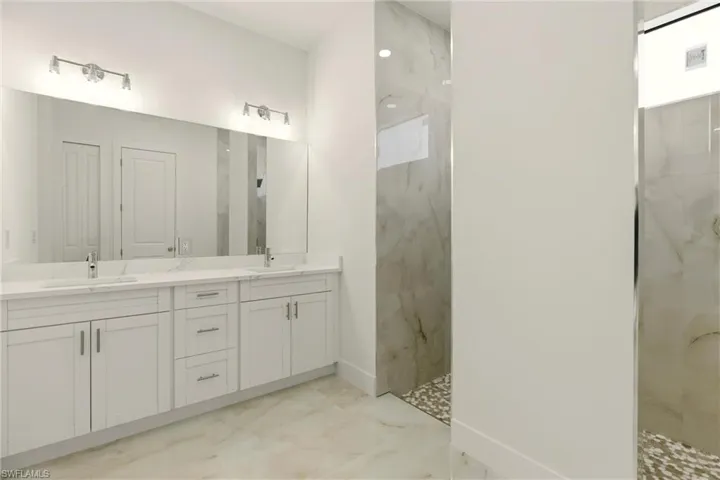 Bathroom with double vanity, a marble finish shower, and light marble finish floors