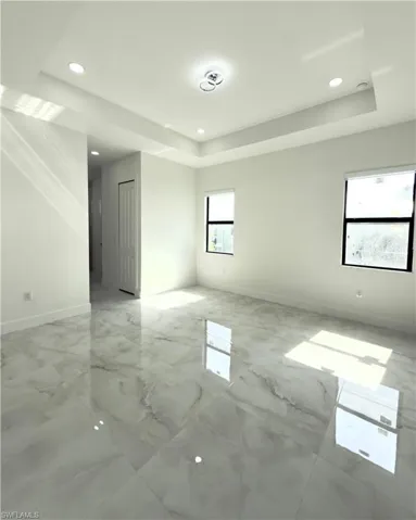 Empty room featuring light marble finish flooring, a raised ceiling, and recessed lighting