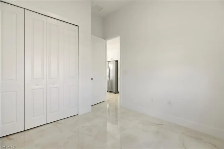 Unfurnished bedroom with freestanding refrigerator, light marble finish floors, and a closet
