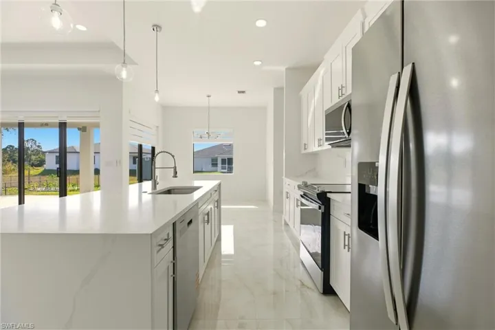 Kitchen with appliances with stainless steel finishes, white cabinetry, decorative light fixtures, light stone countertops, and a large island