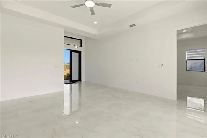 Empty room featuring a raised ceiling, light marble finish flooring, recessed lighting, and ceiling fan