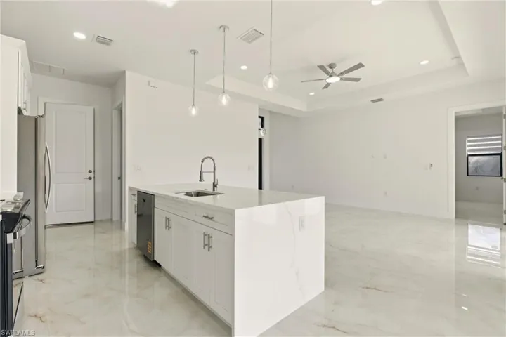 Kitchen with white cabinets, light stone countertops, hanging light fixtures, recessed lighting, and a raised ceiling