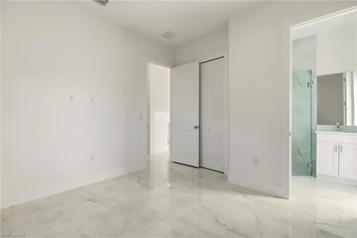 Unfurnished bedroom featuring connected bathroom, light marble finish flooring, and a closet