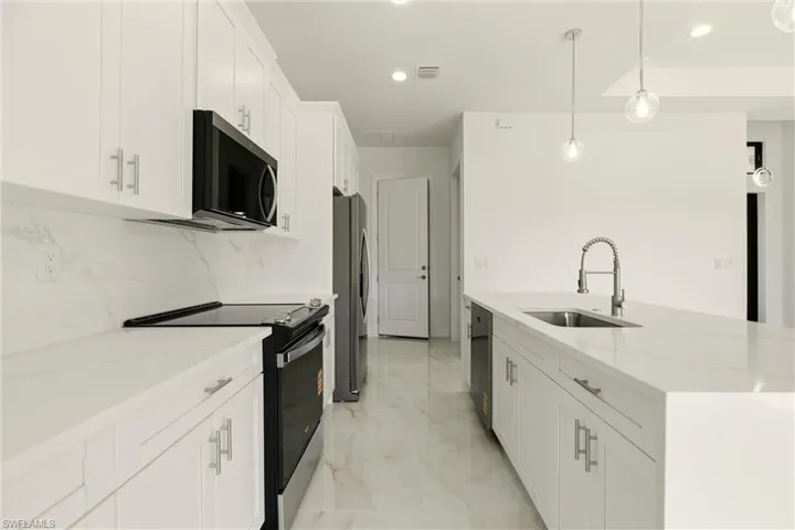 Kitchen with appliances with stainless steel finishes, white cabinetry, pendant lighting, light stone countertops, and recessed lighting
