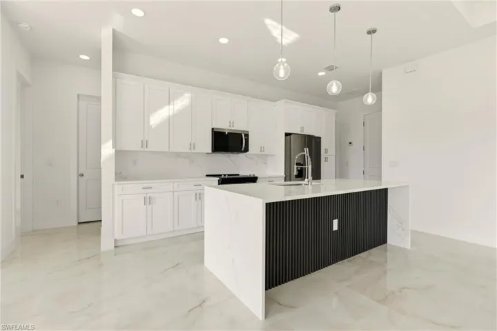 Kitchen with hanging light fixtures, white cabinetry, stainless steel appliances, light stone countertops, and decorative backsplash