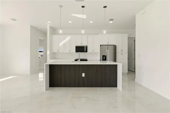 Kitchen with stainless steel fridge, light stone countertops, an island with sink, white cabinets, and pendant lighting
