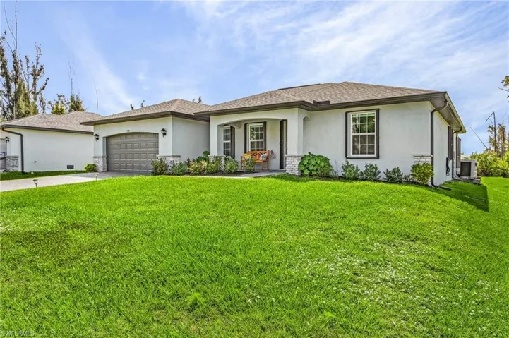 View of front of property with stucco siding, a front lawn, driveway, and a garage