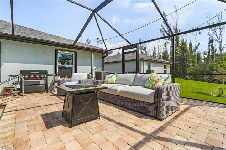View of patio featuring screen enclosure, an outdoor living space with a fire pit, and area for grilling