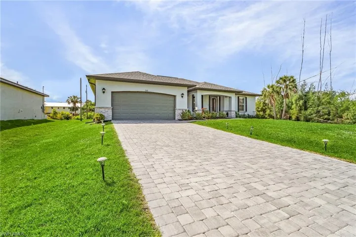 Florida-style home featuring stucco siding, a front yard, decorative driveway, an attached garage, and covered porch