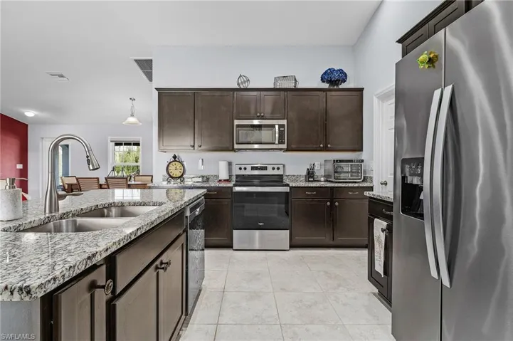 Kitchen featuring stainless steel appliances, dark wood cabinetry, light stone countertops, and hanging light fixtures