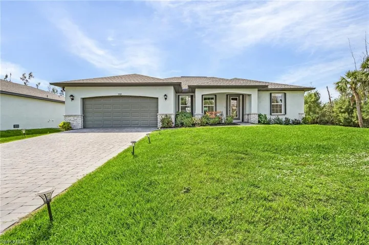 Florida-style home with stucco siding, stone siding, a front lawn, and decorative driveway