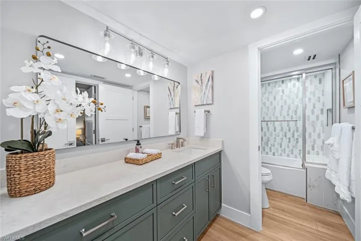 Full bathroom featuring enclosed tub / shower combo, vanity, toilet, and wood-style floors
