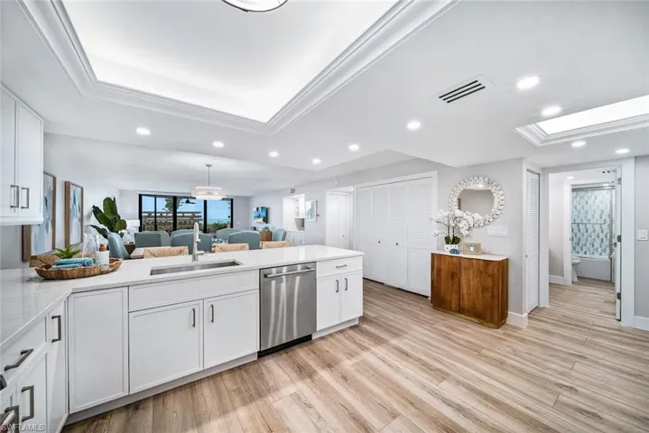 Kitchen featuring light quartz countertops, light wood-style flooring, stainless steel dishwasher, white cabinets, and sink