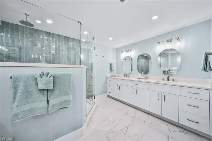 Bathroom featuring dual bowl vanity, tile flooring, and a glass enclosed shower