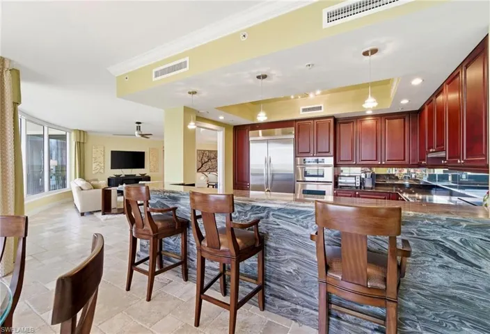 Kitchen with a raised ceiling, pendant lighting, a kitchen breakfast bar, reddish brown cabinets, and dark stone counters