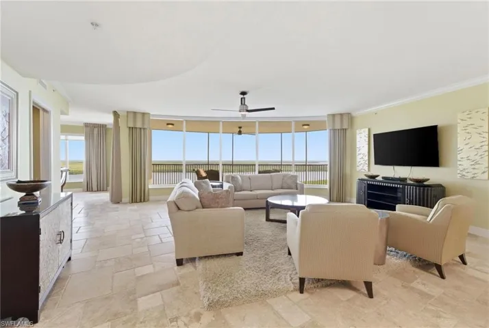 Living room featuring healthy amount of natural light, a wall of windows, ornamental molding, stone tile floors, and a ceiling fan