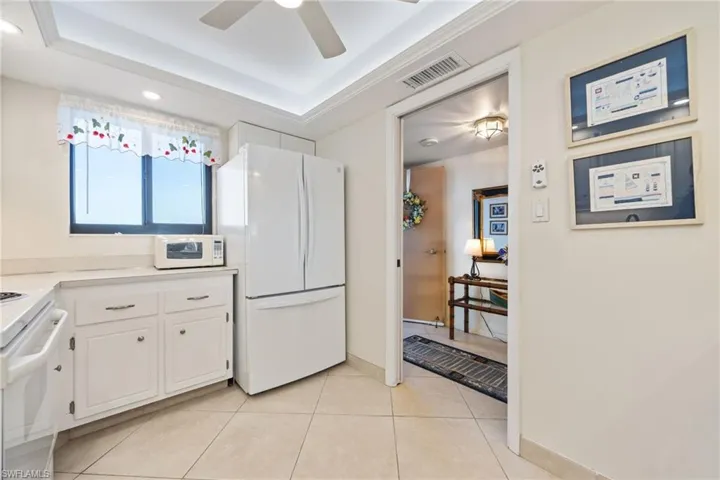 Kitchen featuring white appliances, white cabinets, light countertops, a tray ceiling, and light tile patterned floors