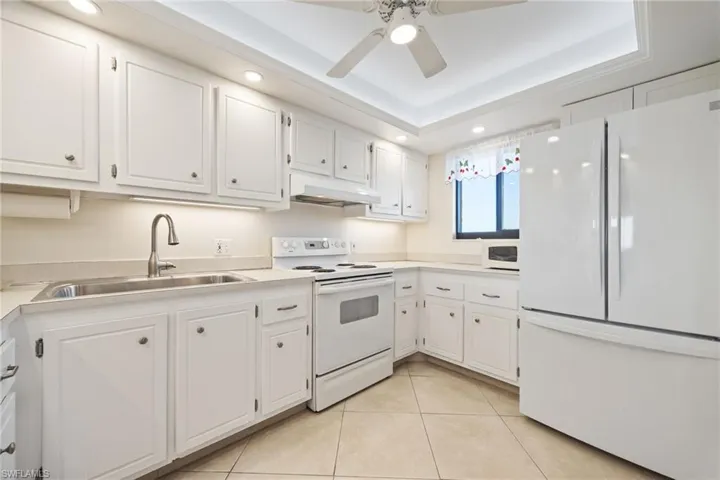 Kitchen featuring white appliances, white cabinets, light countertops, ceiling fan, and a raised ceiling