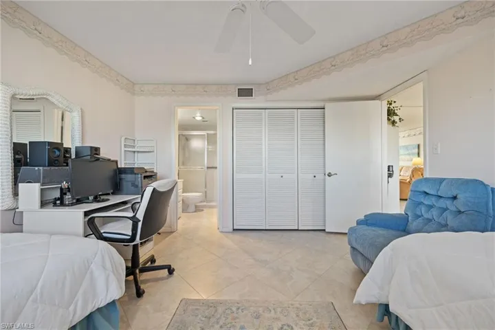 Tiled bedroom featuring a desk, a ceiling fan, a closet, and ensuite bathroom