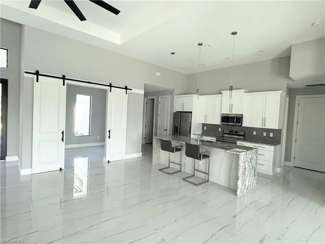 Kitchen featuring dark stone countertops, a barn door, appliances with stainless steel finishes, and a center island with sink