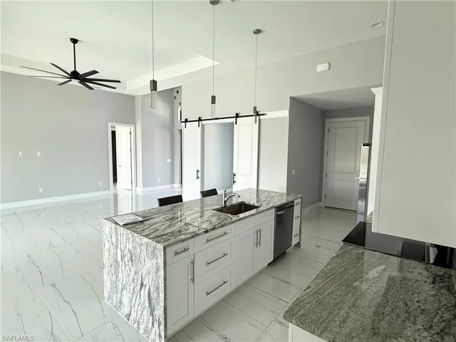 Kitchen with white cabinetry, dishwasher, an island with sink, a barn door, and light stone countertops