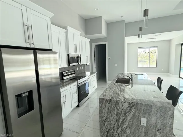 Kitchen featuring pendant lighting, white cabinetry, sink, stainless steel appliances, and a center island with sink