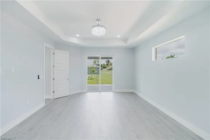 Spacious interior room featuring wood-finish flooring, tray ceiling with recessed lighting and a decorative chandelier, and sliding glass doors opening to the exterior