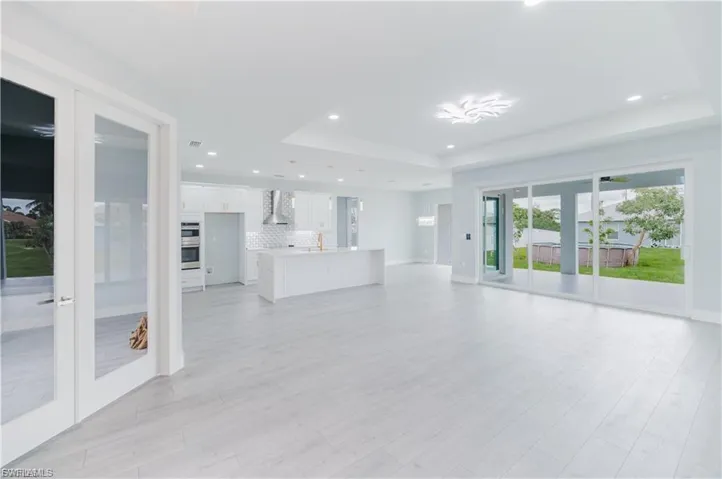 Open-concept living space featuring wood-finish flooring, recessed lighting, and a tray ceiling with a decorative fixture