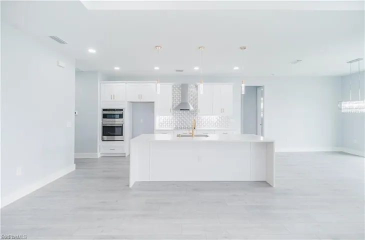 Open-concept kitchen featuring a white center island, coordinating cabinetry, stainless steel double wall ovens, and a decorative tile backsplash