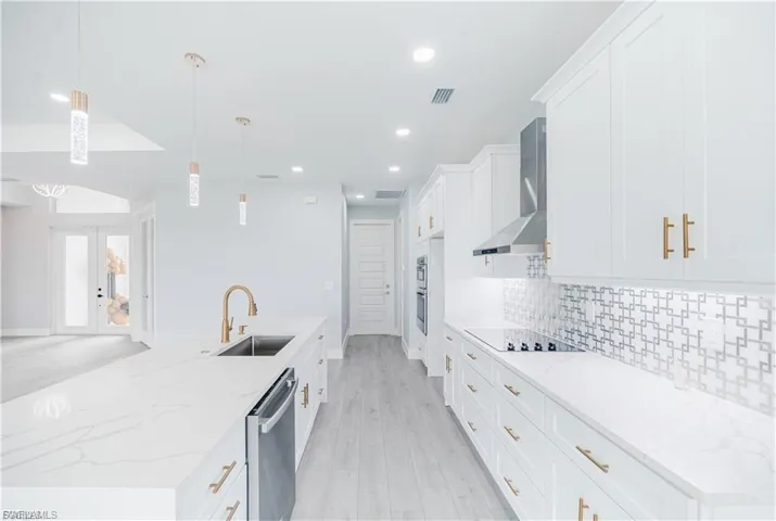Modern kitchen featuring white cabinetry with gold-tone hardware, a large island with an integrated sink and dishwasher, and a patterned tile backsplash