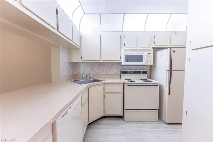 Kitchen featuring light hardwood / wood-style flooring, white appliances, backsplash, sink, and white cabinets