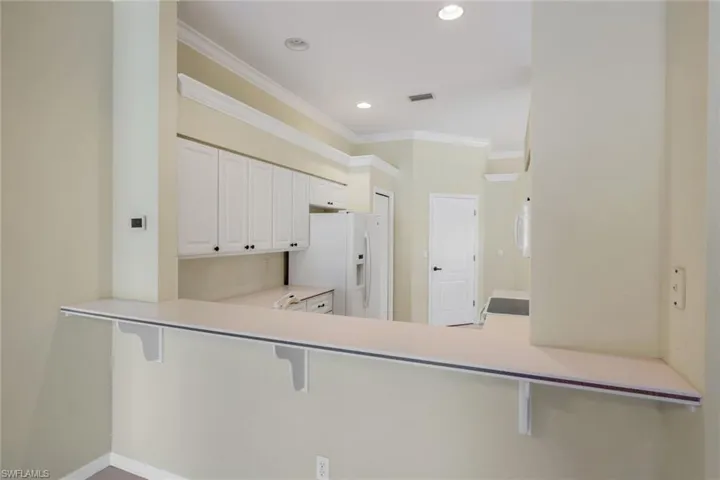 Breakfast bar with support brackets, crown molding, recessed lighting, and white cabinetry with black hardware