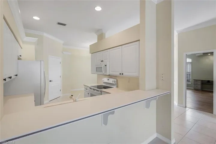 Kitchen featuring white cabinetry, an integrated microwave, recessed lighting, a smooth-top range, and a breakfast bar