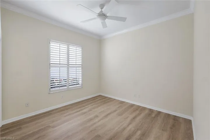 Wood-finish flooring, crown molding, ceiling fan, and window with plantation shutters