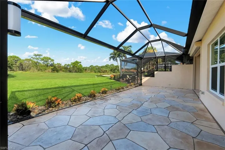 Screened patio with a geometric paver floor, exterior wall lighting, and a landscaped bed