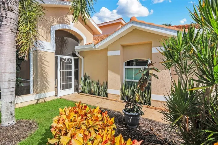 Stucco exterior with a tile roof, arched entry, screened front door, and established landscaping