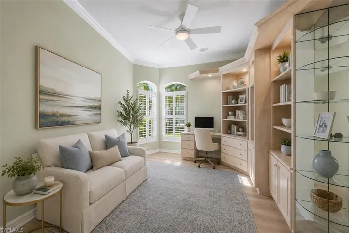 Built-in cabinetry with integrated desk, crown molding, arched windows with plantation shutters, wood-finish flooring, and a ceiling fan