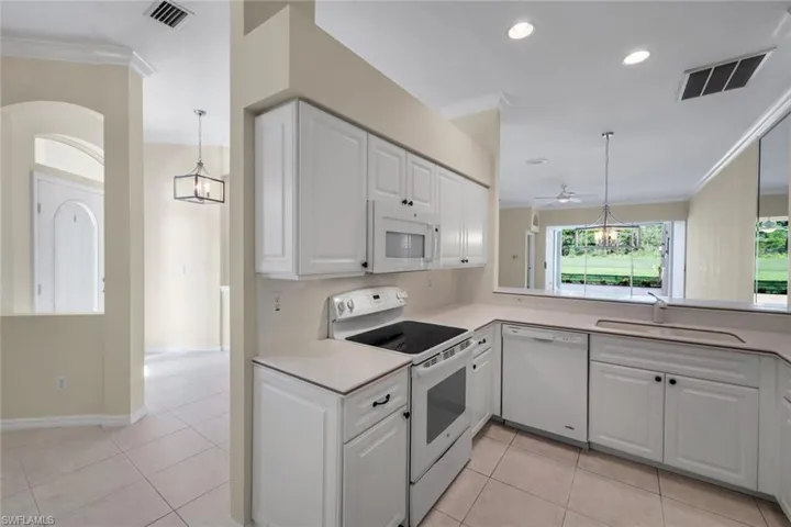 White cabinetry, recessed lighting, tile flooring, built-in microwave, and a stainless steel sink with a single-handle faucet