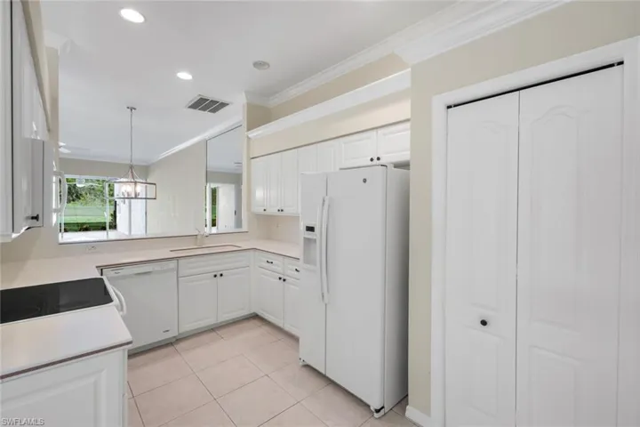Bright, efficiently designed kitchen featuring white cabinetry, tile flooring, stainless steel refrigerator, and recessed ceiling lighting