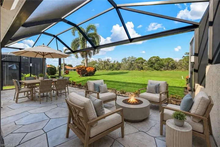Screened lanai featuring a patterned stone patio, integrated fire pit, and expansive green space
